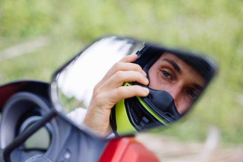 Reflektion im Seitenspiegel eines Quads von einem Mann mit Motorradhelm und Zubehör.
