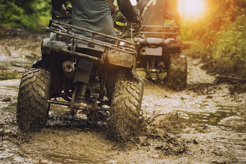 Quads fahren durch Schlamm mit Zubehörsortiment für Kymco ATVs, darunter Schutzbügel, Windschutzscheiben und Gepäcksysteme.
