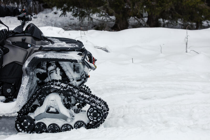 Quad mit montierten Can-Am Raupenkits, das auf verschneitem Gelände fährt.